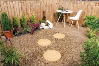 Buff gold stepping stones on a gravel pathway. leading to a white table and chair.