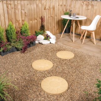 Buff gold stepping stones on a gravel pathway. leading to a white table and chair.