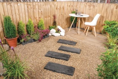charcoal rustic stone lifestyle shot. 4 Charcoal coloured stepping stones on an earth coloured gravel pathway. The stepping stones llead to a white table and chair