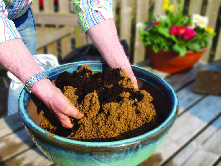 Two hands mixing horticultrual sharp sand in a blue ceramic bowl